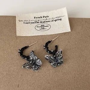 Close-up detail of dark liquid-style earrings featuring transparent resin butterfly charms.