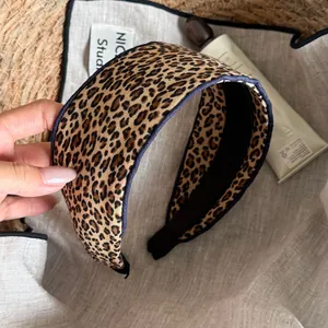 Close-up view of a leopard print fabric headband on a natural linen and straw background