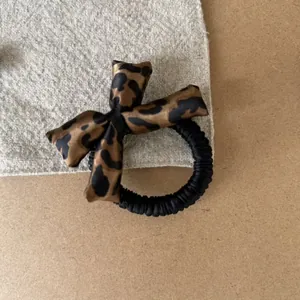 Close-up view of a vintage leopard print sponge bow on a black elastic hair scrunchie