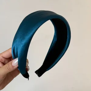 Close-up view of a padded teal satin headband held by a hand to show its thickness and texture.
