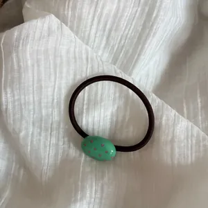 Primer plano de una goma de pelo negra con un adorno ovalado verde de lunares rosas