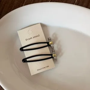 Détail rapproché de barrettes à cheveux minimalistes en métal argenté mat sur carte