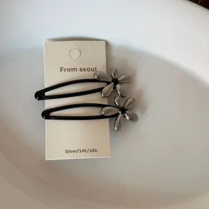 Détail de pinces à cheveux fleurs noir mat et argenté sur présentoir.