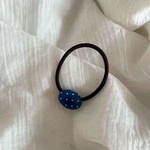 Primer plano de una cuenta ovalada azul con lunares en un coletero negro elástico