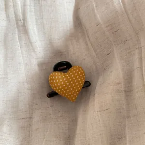 Detailed macro shot of yellow polka dot heart-shaped hair claw clip on fabric.