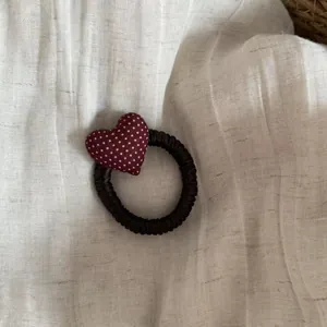 Detail view of a burgundy polka dot heart hair tie on cream linen background