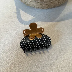 Dettaglio di un elegante fermaglio per capelli a pois neri con manico a fiore marrone.
