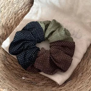 Détail du chouchou en tissu à pois tricolore sur fond de sac en lin naturel.