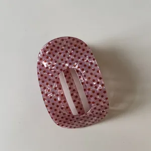 Gedetailleerde opname van een roze ovale haarklem met rode stippen en acryl textuur.