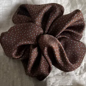 Detailed view of elegant brown polka dot scrunchie hair accessory on a beige linen background
