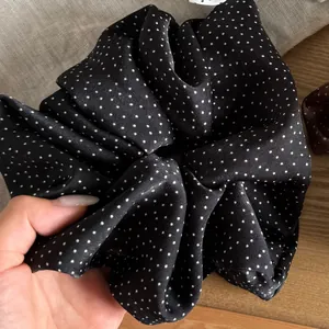 Detailed macro view of a soft black satin scrunchie featuring a white star polka dot pattern