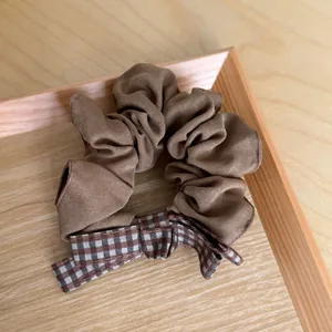 Detailed view of a brown fabric scrunchie featuring a retro plaid bow on a wooden tray