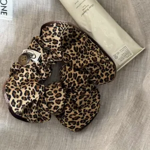 Close-up detail of a Korean style leopard print scrunchie with a button and Blazing tag