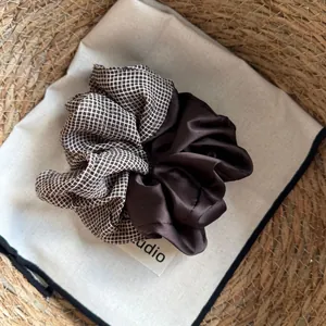 Detail shot of a brown scrunchie featuring grid patterns and smooth satin textures