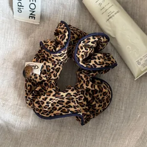 Close-up of leopard print scrunchie with navy blue piping and decorative button