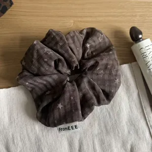 Close-up detail of a brown plaid scrunchie featuring white star patterns and a small brand tag