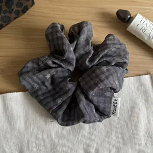 Detailed view of a dark grey plaid scrunchie with subtle star patterns on wood surface