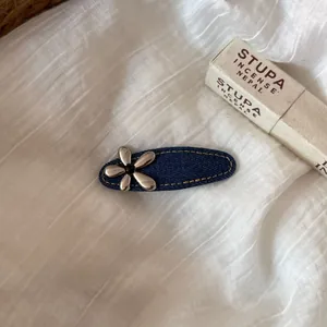 Vue détaillée de la pince à cheveux bleu denim avec fleur en métal argenté sur lin blanc