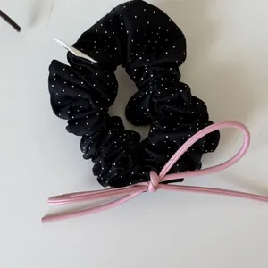 Close-up of black polka dot scrunchie featuring a pink faux leather bow accent