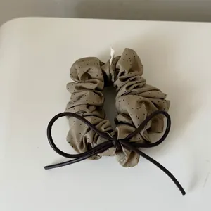 Detail of a khaki polka dot scrunchie featuring a brown leather-like bow knot.