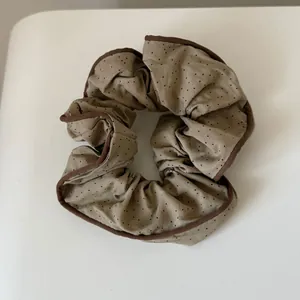 Macro detail of a brown polka dot pleated fabric scrunchie hair tie for women