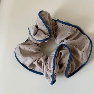 Close-up detail of beige polka dot fabric scrunchie with navy blue ruffled piping edge