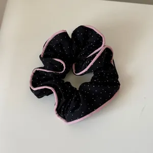 Detailed view of a black polka dot scrunchie featuring elegant pink ruffled piped edges