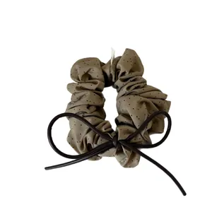 Polka dot ruffled scrunchie with a dark brown leather bow on a clean white background