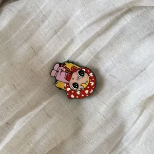 Detailed view of a cute retro girl enamel pin with a red heart scarf on a cream linen cloth