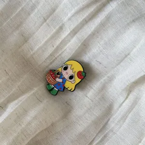 Detailed macro shot of a cartoon girl enamel pin with a strawberry basket on linen