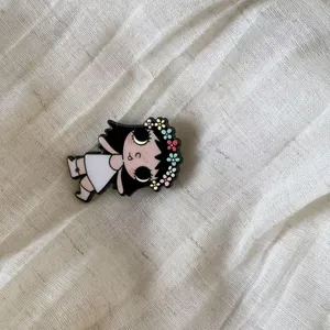 Detailed macro view of a cute cartoon girl enamel pin with a colorful flower crown on white linen