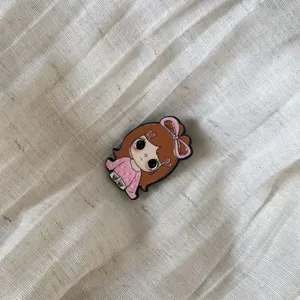 Detailed macro shot of a cute cartoon girl enamel pin featuring a large pink bow decoration