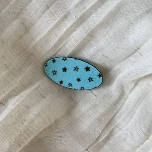 Close-up of light blue acetate hair clip with black star pattern on linen background