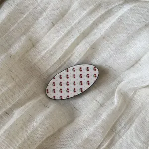 Macro view of vintage oval hair clip with cute red cherry pattern on linen texture.
