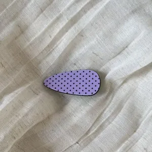 Close-up of purple teardrop hair clip with black star pattern on linen background