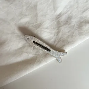 Detalle de una pinza para el pelo plateada con purpurina en forma de pez y un pequeño ojo de cristal