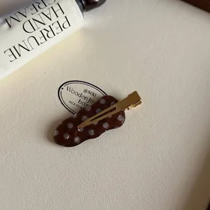 Detail van een bruine acetaat haarklem met witte stippen en een gouden metalen clip.