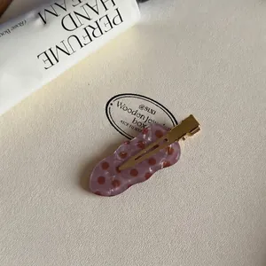 Detailopname van de roze-bruine gestippelde acetaat haarklem op een witte lederen achtergrond.