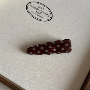 Detailopname van een bruine gegolfde acetaat haarklem met wit polkadot patroon