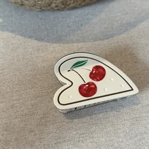Detailed macro view of a cream heart-shaped acetate hair claw clip with a red cherry motif