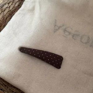 Vue détaillée d'une barrette à cheveux marron à pois sur un sac en lin naturel.