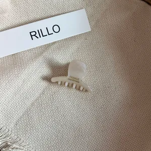 Detailed view of a cream-colored acetate mini hair claw clip on a textured beige fabric