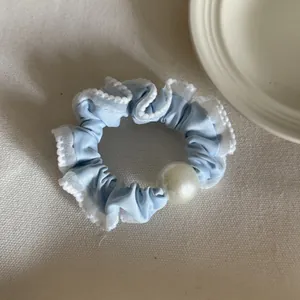 Detailopname van een lichtblauwe ruches scrunchie met een grote elegante witte parel