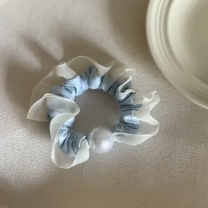 Detail van een lichtblauwe en witte geplooide scrunchie met een grote decoratieve parel