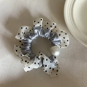 Detail van een scrunchie met stippen, grijs satijn en een grote witte parel decor.