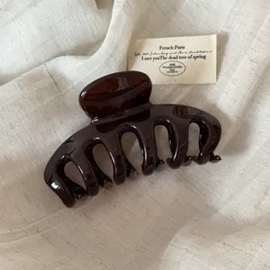 Close-up of a glossy dark brown hair claw clip resting on a soft cream fabric background