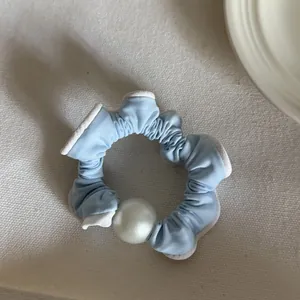 Detailopname van een lichtblauwe scrunchie met een grote witte parel op stof