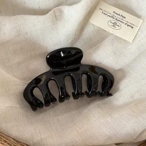 Detail macro view of a large glossy black dragon-bone hair claw clip on linen fabric.