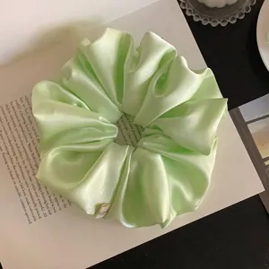 Detailed macro view of a light green satin scrunchie showing elegant pleated fabric