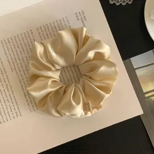 Close-up of champagne satin scrunchie with bow detail on open book background.